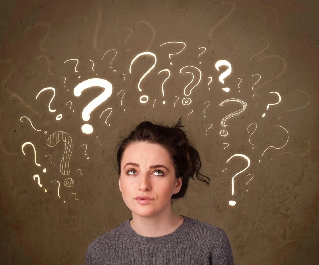 A woman looks upward with a thoughtful expression as multiple illuminated question marks appear around her on a brown background—perfect inspiration for clever IG captions.