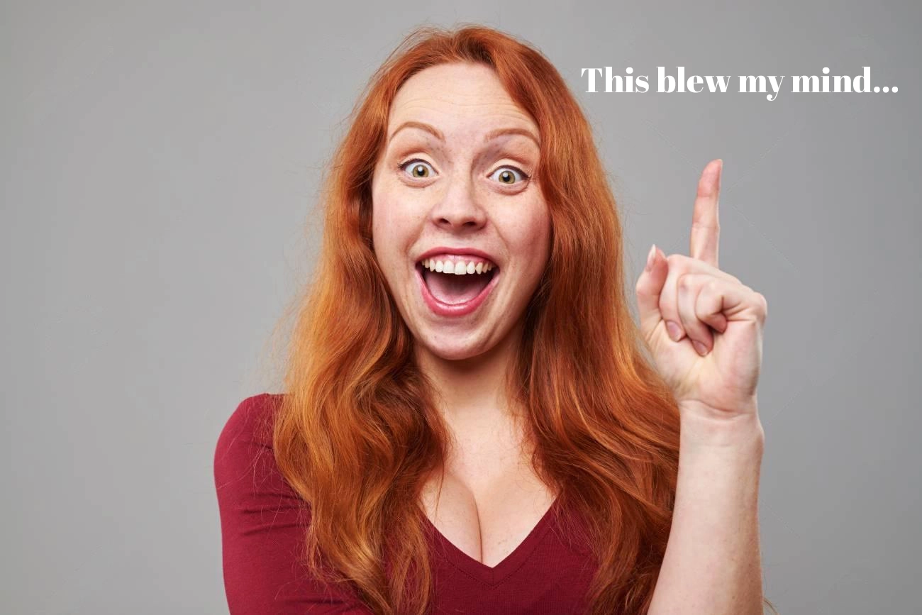 A woman with long red hair and a maroon shirt smiles widely and points upward; white text reads,"This blew my mind... IG Captions" on a plain gray background.