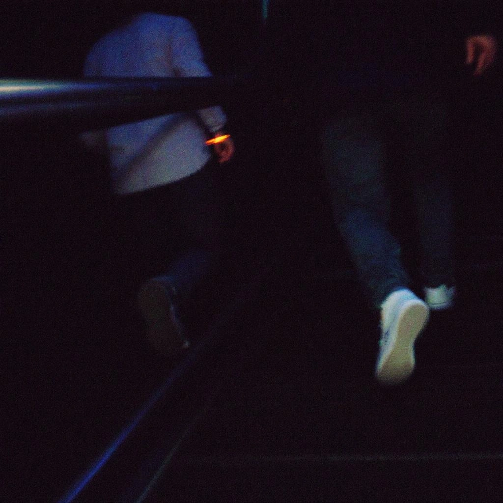 Two people are walking up a dark staircase; one in a light shirt, the other in a dark outfit, both partially out of frame—an intriguing scene that exemplifies detailed image descriptions.
